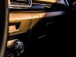 A close-up view of a car's interior dashboard, featuring a clean and sleek design. The image highlights a climate control knob with the word 'DUAL' inscribed on it, surrounded by metallic and glossy surfaces. The lighting creates a warm glow across the dashboard.