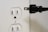 A white electrical outlet with two sockets is positioned on the left side. Near it is a black electrical plug with two prongs oriented towards the outlet, suggesting a connection is about to be made.