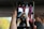 A person is taking a selfie with a digital camera, reflected on the screen of a smartphone. The setting appears to be inside a red vehicle, with windows and part of the interior visible. The smartphone is held by someone's hand, capturing the reflection.
