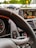 The interior of a car with a focus on the steering wheel, dashboard, and digital display. The digital display is showing a list of radio stations with the current selection highlighted. The start-stop engine button is visible near the steering wheel, which has a black and red design.