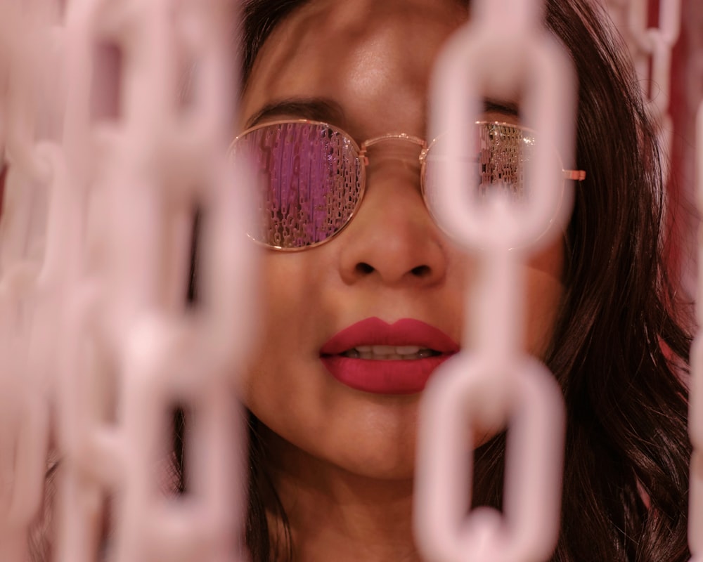 a woman wearing glasses looking through a chain link fence