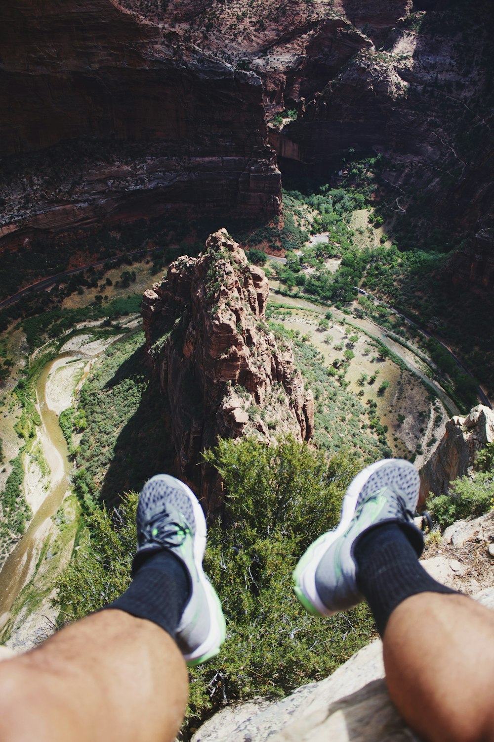 person sitting on cliff near mountains and grass field