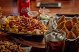 A platter featuring a variety of loaded fries with dinosaur-shaped dipping sauces in vibrant bowls.