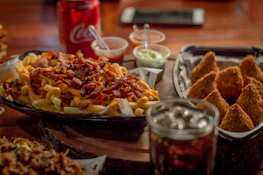 A colorful spread of munchies including fries, burgers, and dips under warm lighting.