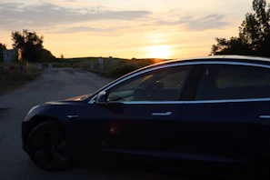Sleek black sedan parked on a coastal road at sunset