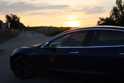 A sleek security vehicle driving along a quiet road near a high-end residential estate during sunset.