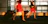 The image captures a motion blur of flight attendants in red uniforms walking briskly through an airport terminal, pulling black rolling luggage. The setting is modern with large glass windows allowing natural light to flood in, casting shadows on the floor.