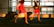 The image captures a motion blur of flight attendants in red uniforms walking briskly through an airport terminal, pulling black rolling luggage. The setting is modern with large glass windows allowing natural light to flood in, casting shadows on the floor.