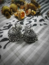 A pair of trendy jhumkas with intricate detailing displayed on a minimalist ivory background.