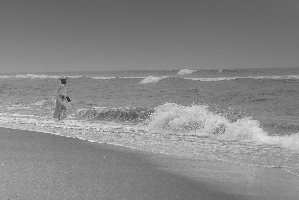 grayscale photo of man walking on seashore