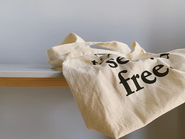 A close-up of a sturdy canvas tote bag with leather handles resting on a wooden table.