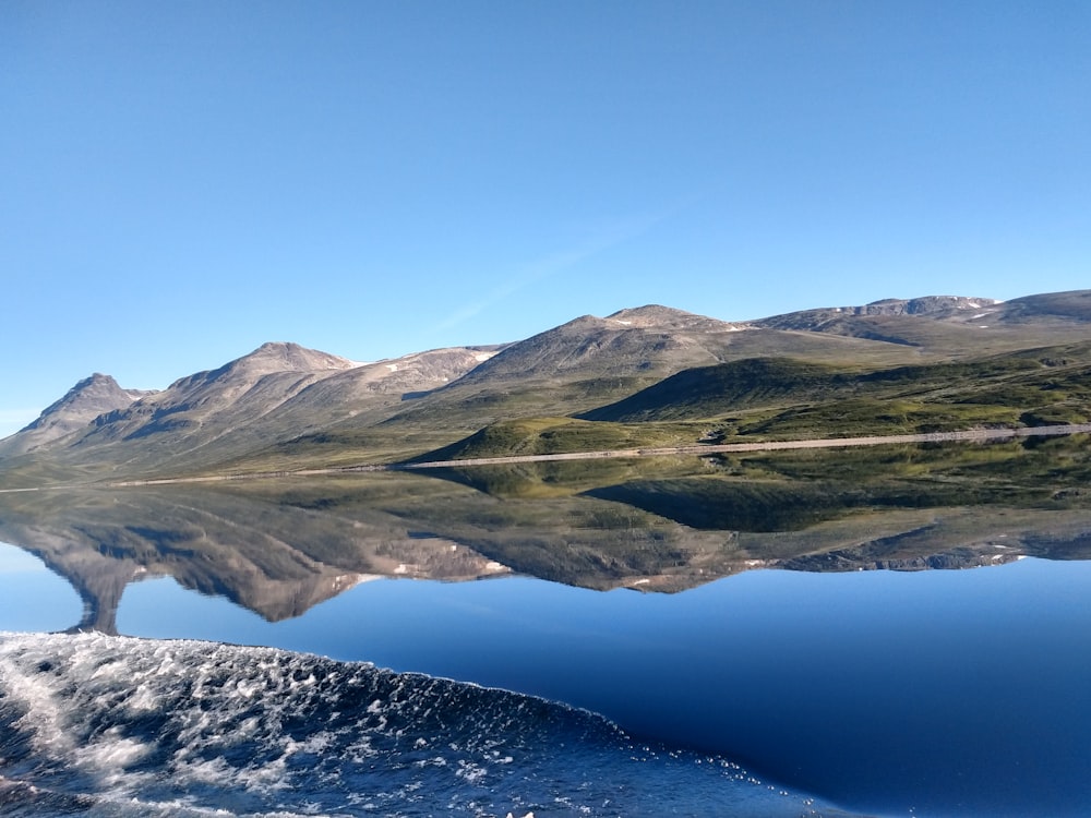 reflection of green mountains on body of water during daytime