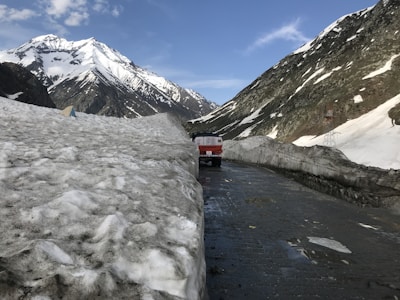 A modern refrigerated truck driving along a scenic mountain road under a clear blue sky.