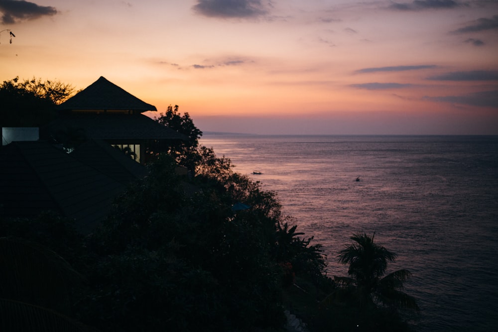 a sunset over the ocean with a house on the cliff