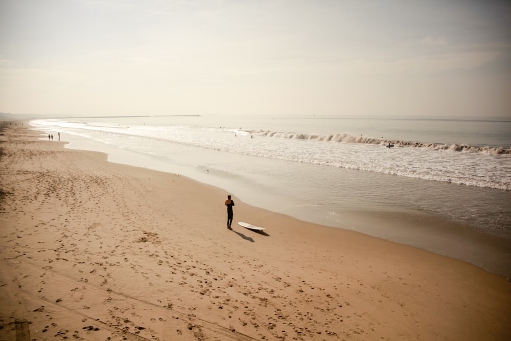 uma pessoa em pé em uma praia com uma prancha de surf