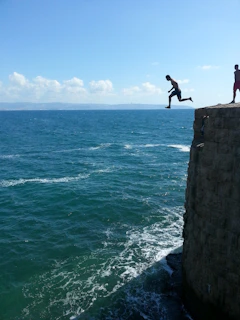 A panoramic view of a cliff diving spot with a fearless jumper mid-air.