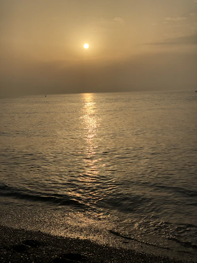 A golden sunset casting warm light over a calm tropical beach with gentle waves.
