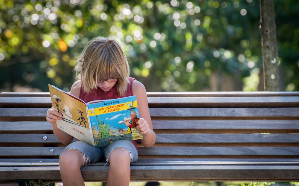 girl in red top sitting on bench while reading