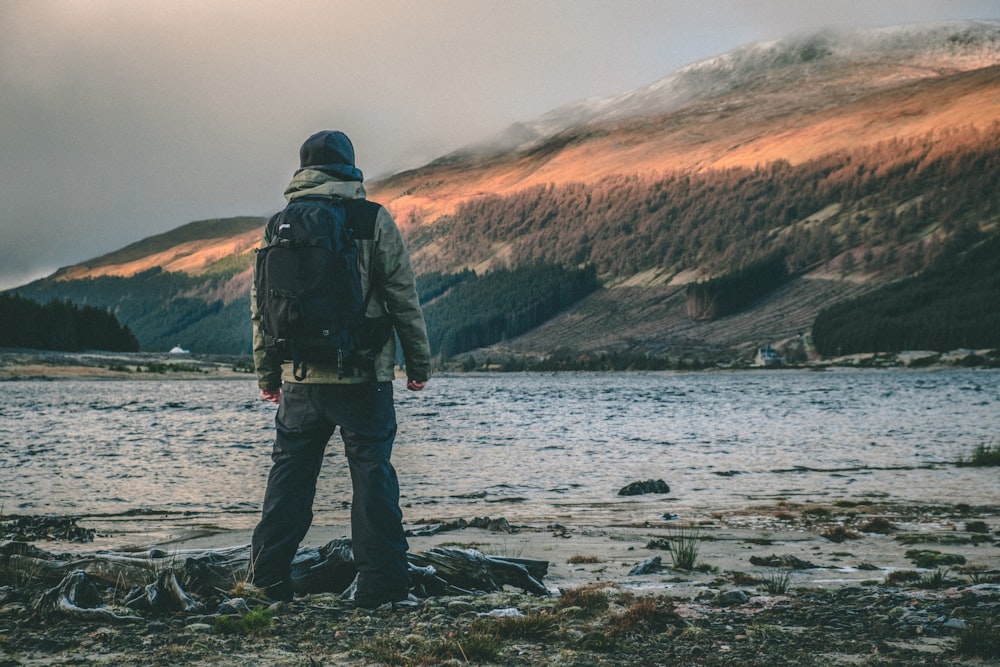 person standing and facing on lake near mountain