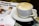 A cup of coffee with frothy milk sits on a saucer accompanied by a teaspoon. Next to it is a magazine or brochure titled 'Medical Conference Planning' featuring an image of two people in conversation, likely in a professional or clinical setting.