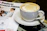 A cup of coffee with frothy milk sits on a saucer accompanied by a teaspoon. Next to it is a magazine or brochure titled 'Medical Conference Planning' featuring an image of two people in conversation, likely in a professional or clinical setting.