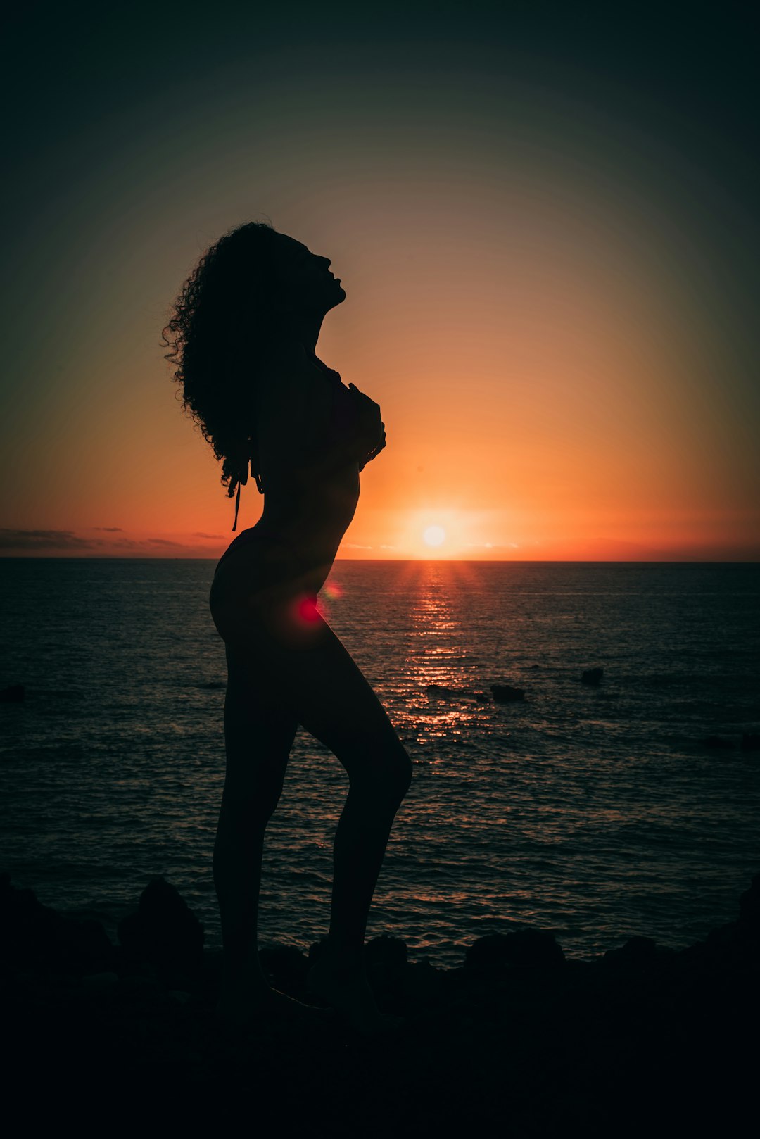 silhouette of woman standing beside sea during golden hour