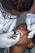 A dentist wearing glasses and gloves is performing a dental procedure on a child. The dentist is using dental instruments, and the child's mouth is open.