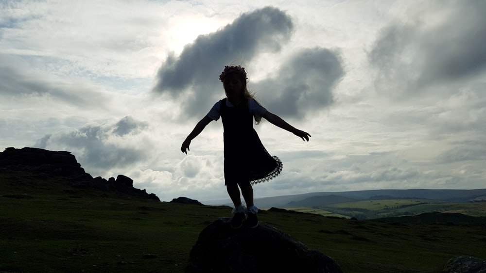 silhouette of girl in dress standing on boulder during daytime