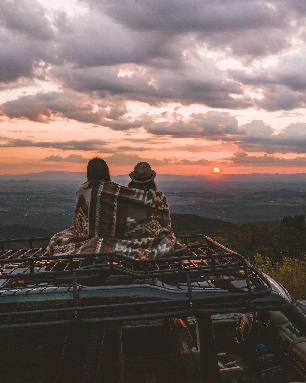 two people sitting on vehicle roof during golden hour