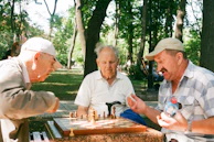 A group of senior citizens playing chess while kids watch and cheer them on.