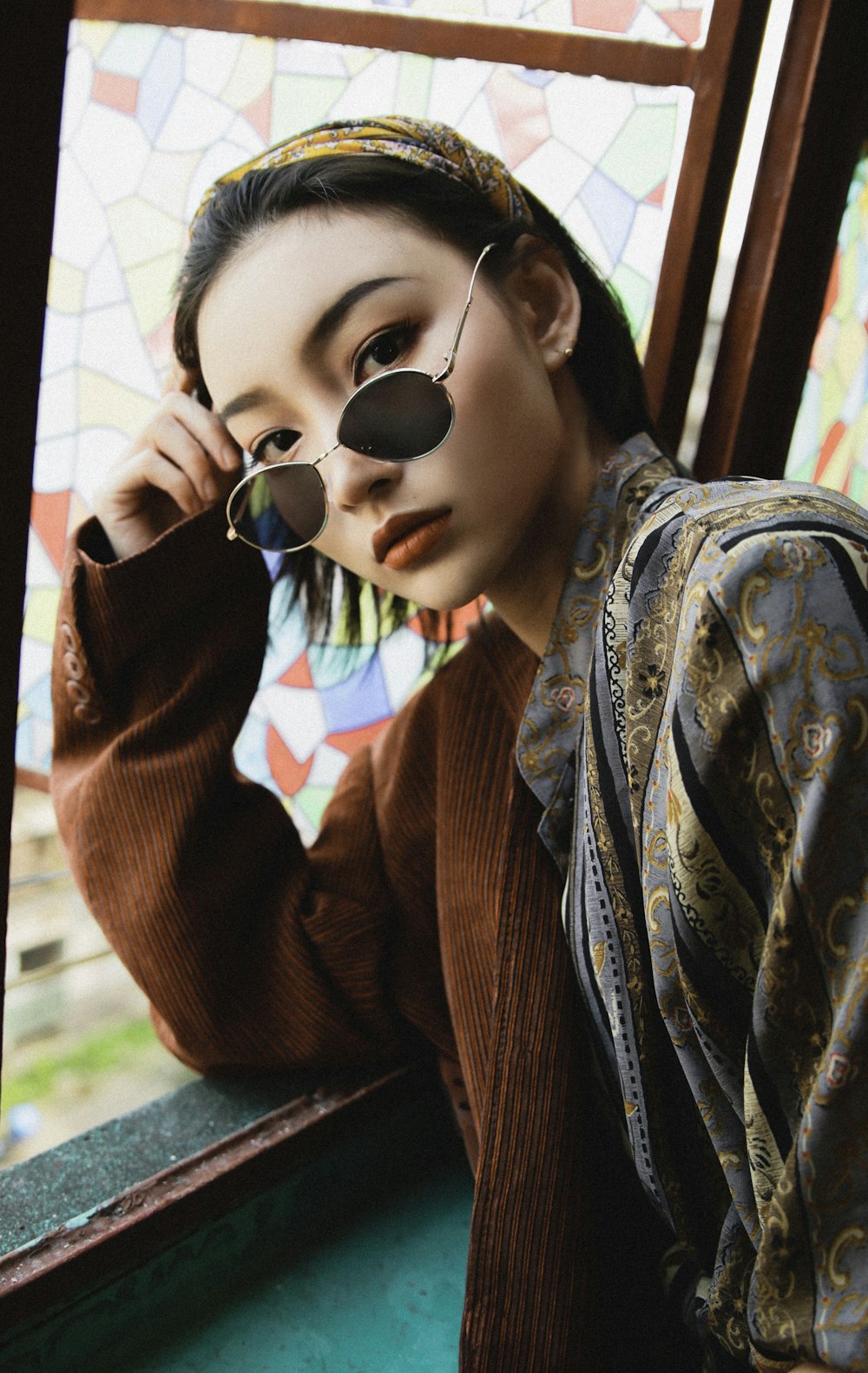 woman wearing brown coat and round grey framed black lens sunglasses