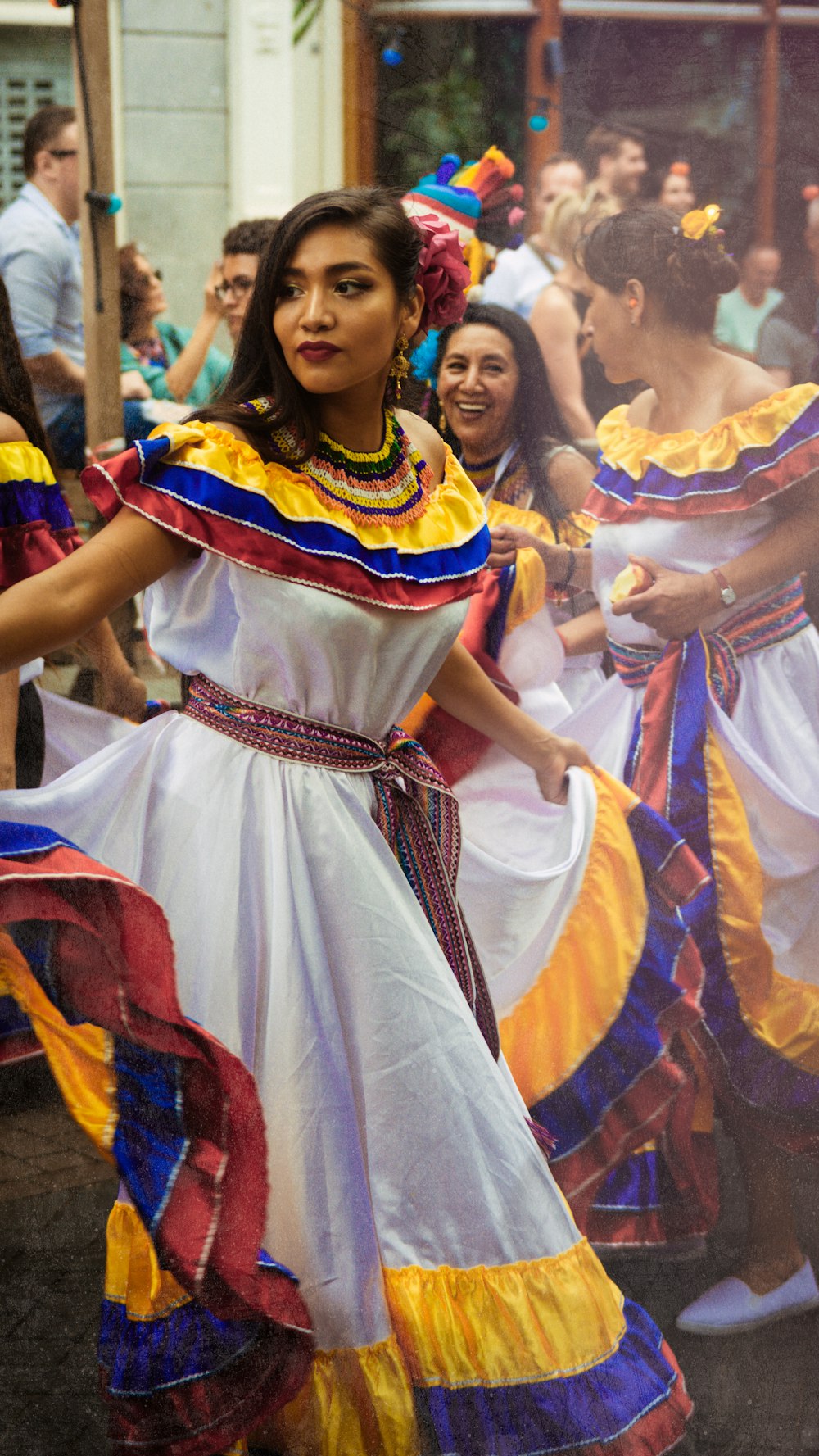 women wearing multicolored dresses dancing on street surrounded with people