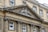A historic stone building facade with classical architectural elements. An ornate pediment features a heraldic emblem and the inscription 'Royal Mineral Water Hospital'. Large, symmetrical windows are supported by decorative columns.