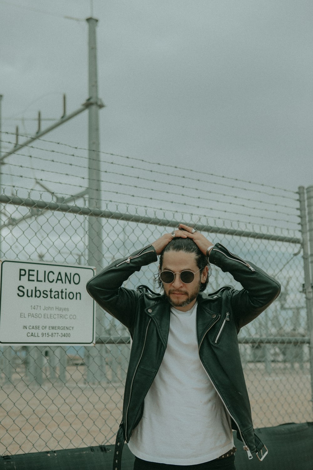 man wearing black leather jacket standing beside chain link fence