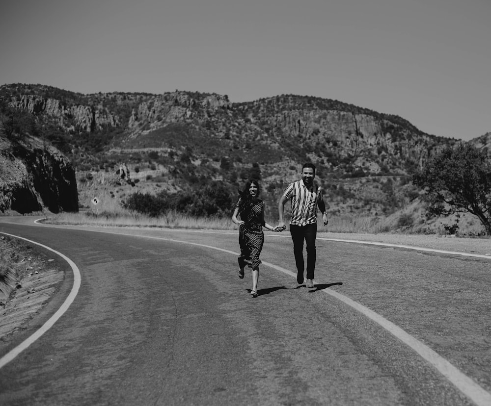 grayscale photography of man and woman holding hands while running on road