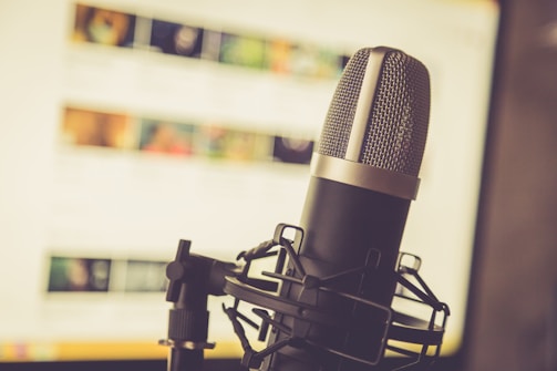 A professional microphone is positioned in the foreground, with a soft focus background showing a computer screen displaying various blurred images and text.