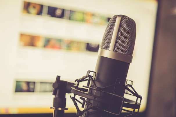 A professional microphone is positioned in the foreground, with a soft focus background showing a computer screen displaying various blurred images and text.