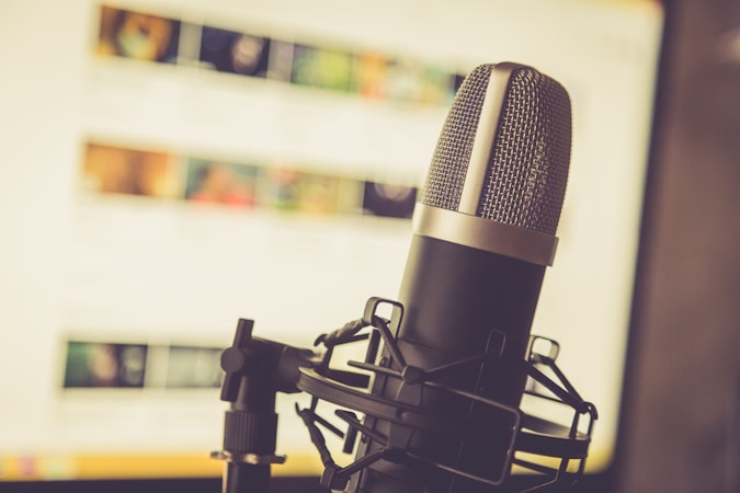 A professional microphone is positioned in the foreground, with a soft focus background showing a computer screen displaying various blurred images and text.