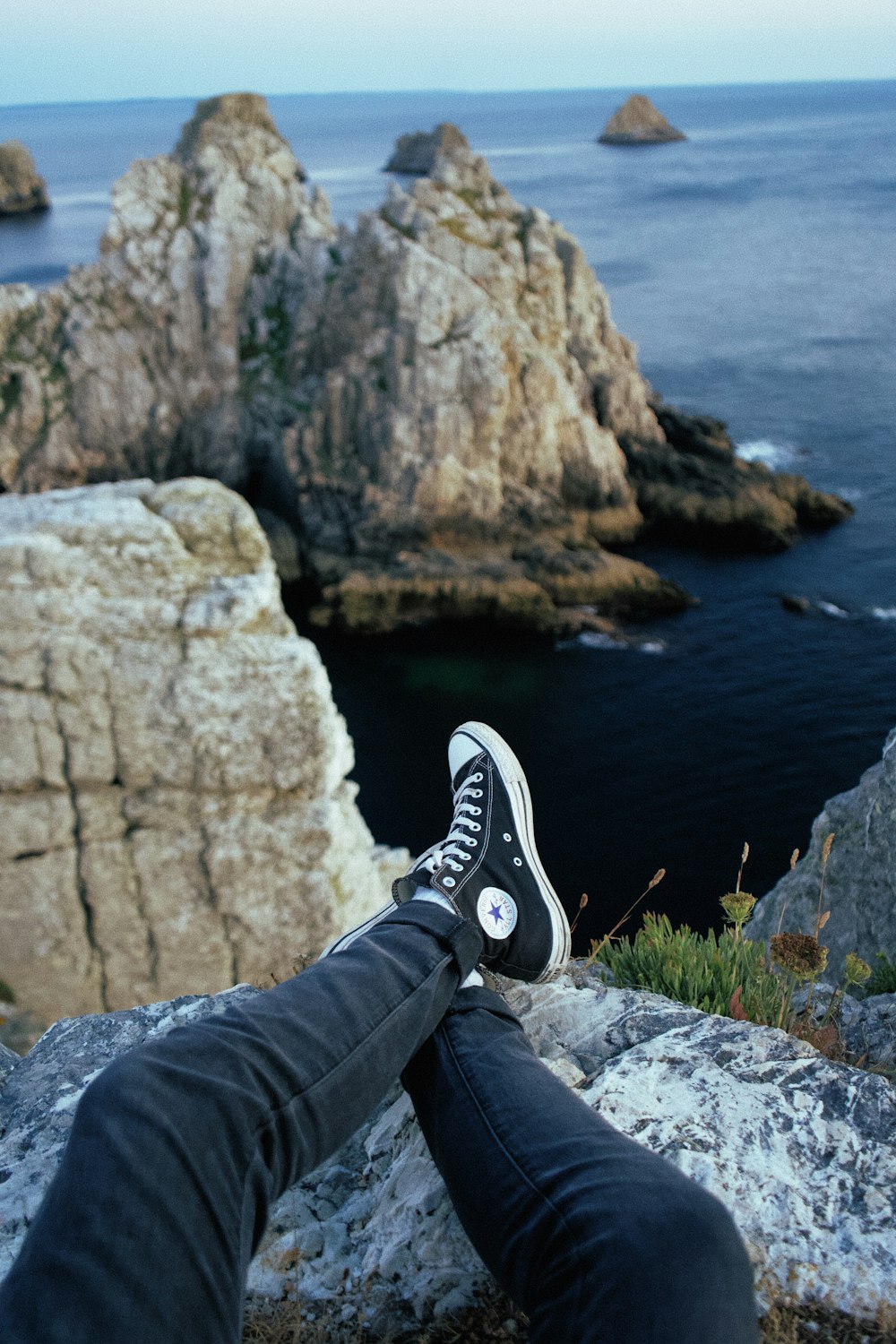Foto persona jeans azules y un par de zapatillas Converse All-Star negras de gran altura sobre rocas marrones – Imagen Mar en Unsplash