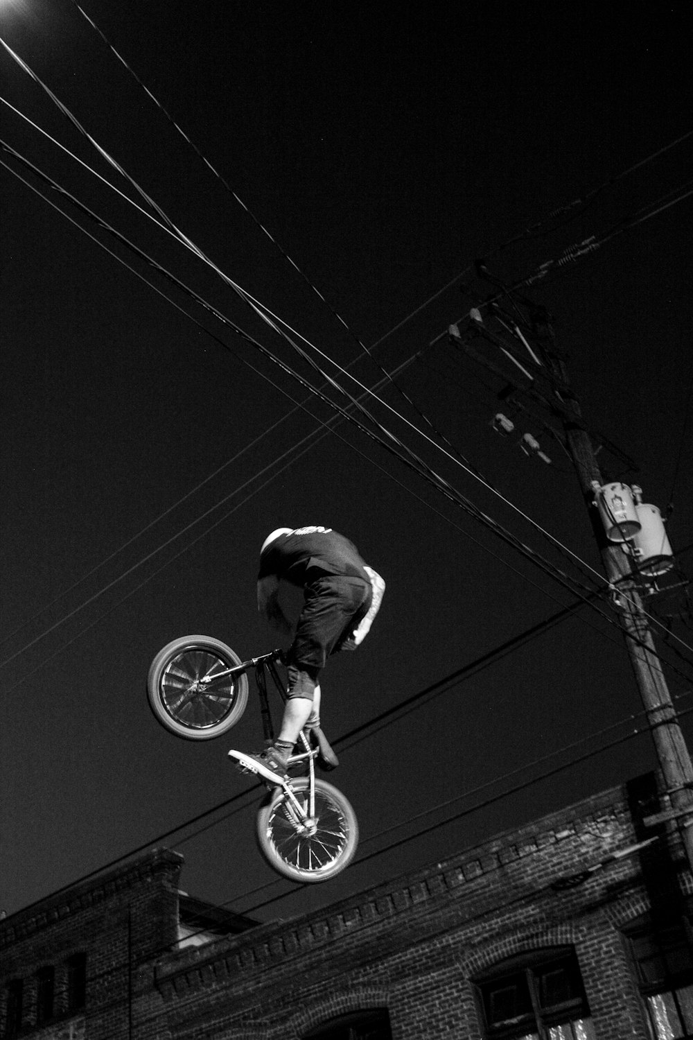 grayscale photo of man riding BMX bicycle on air