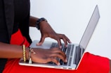 A close-up of hands typing on a laptop keyboard with a cross necklace nearby.