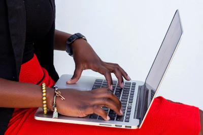 Close-up of hands typing on a laptop with a red-themed header on the screen.