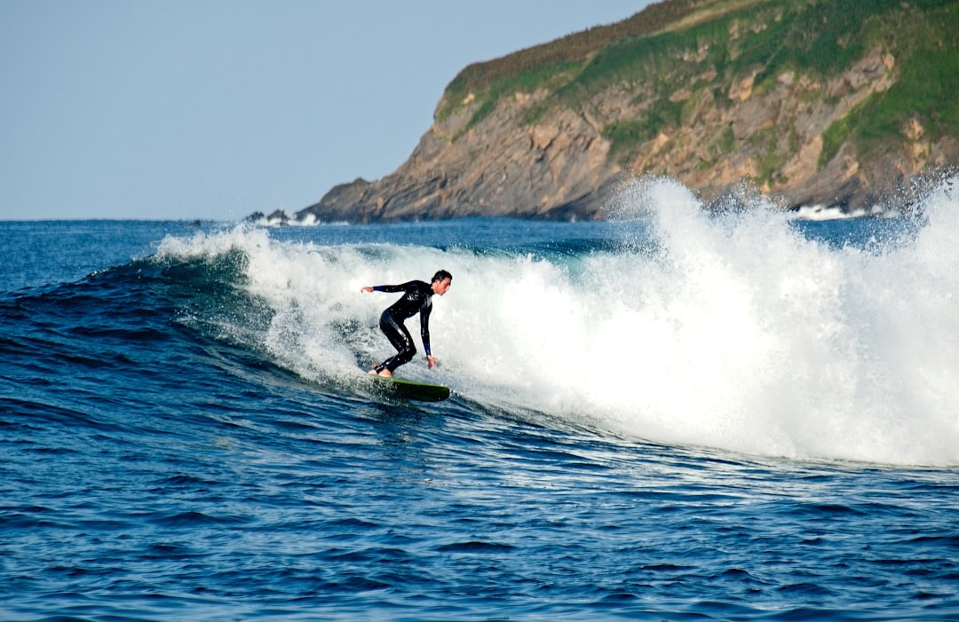 person wearing black wetsuit riding surfboard on body of water