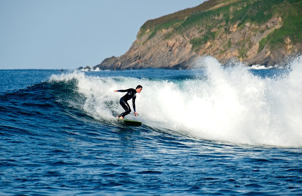 Person im schwarzen Neoprenanzug, die Surfbrett auf dem Gewässer reitet