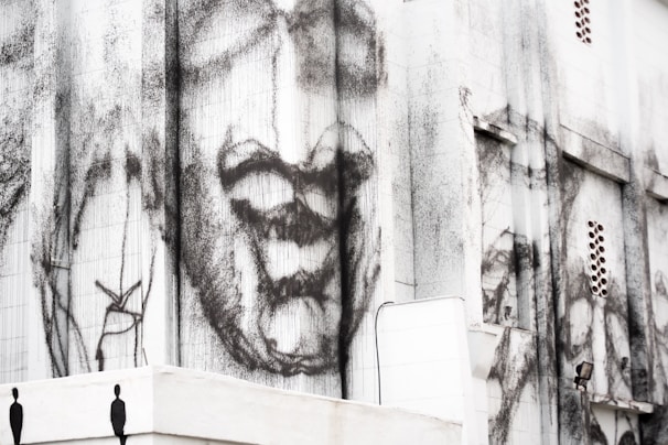 A large building façade featuring abstract and expressive black and white artwork. The artwork appears to depict a face with exaggerated features in an emotive style, adding a dramatic and thought-provoking element to the urban environment.