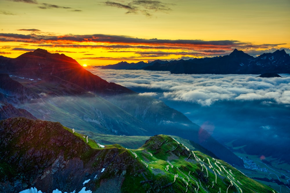 the sun is setting over the mountains above the clouds