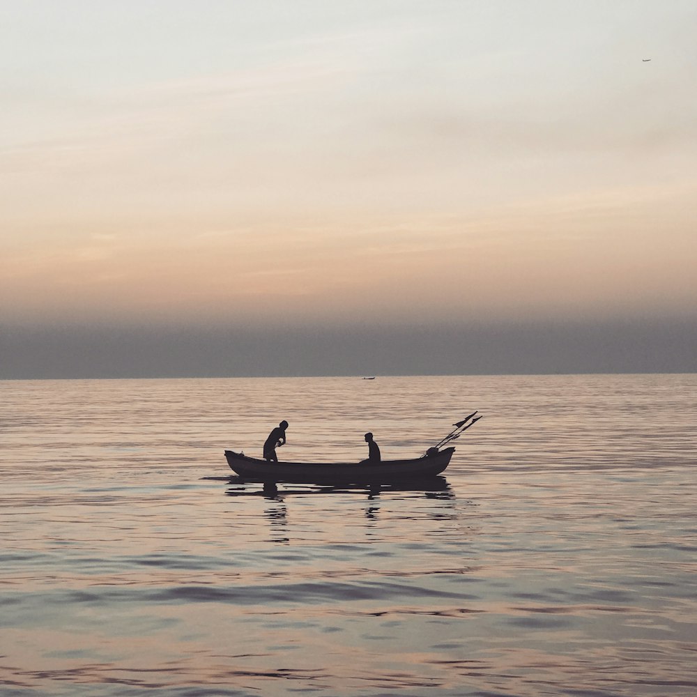 two person in boat on sea under orange and blue skies