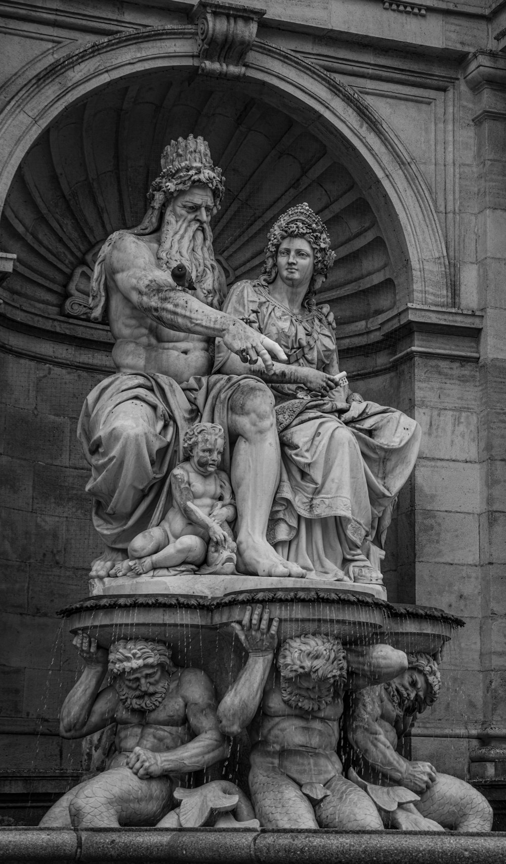 grayscale photography of man and woman with toddler sitting above platform held by men statue
