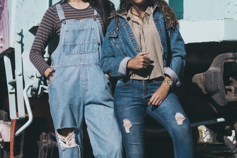 two women standing side by side wearing denim dungarees and jacket