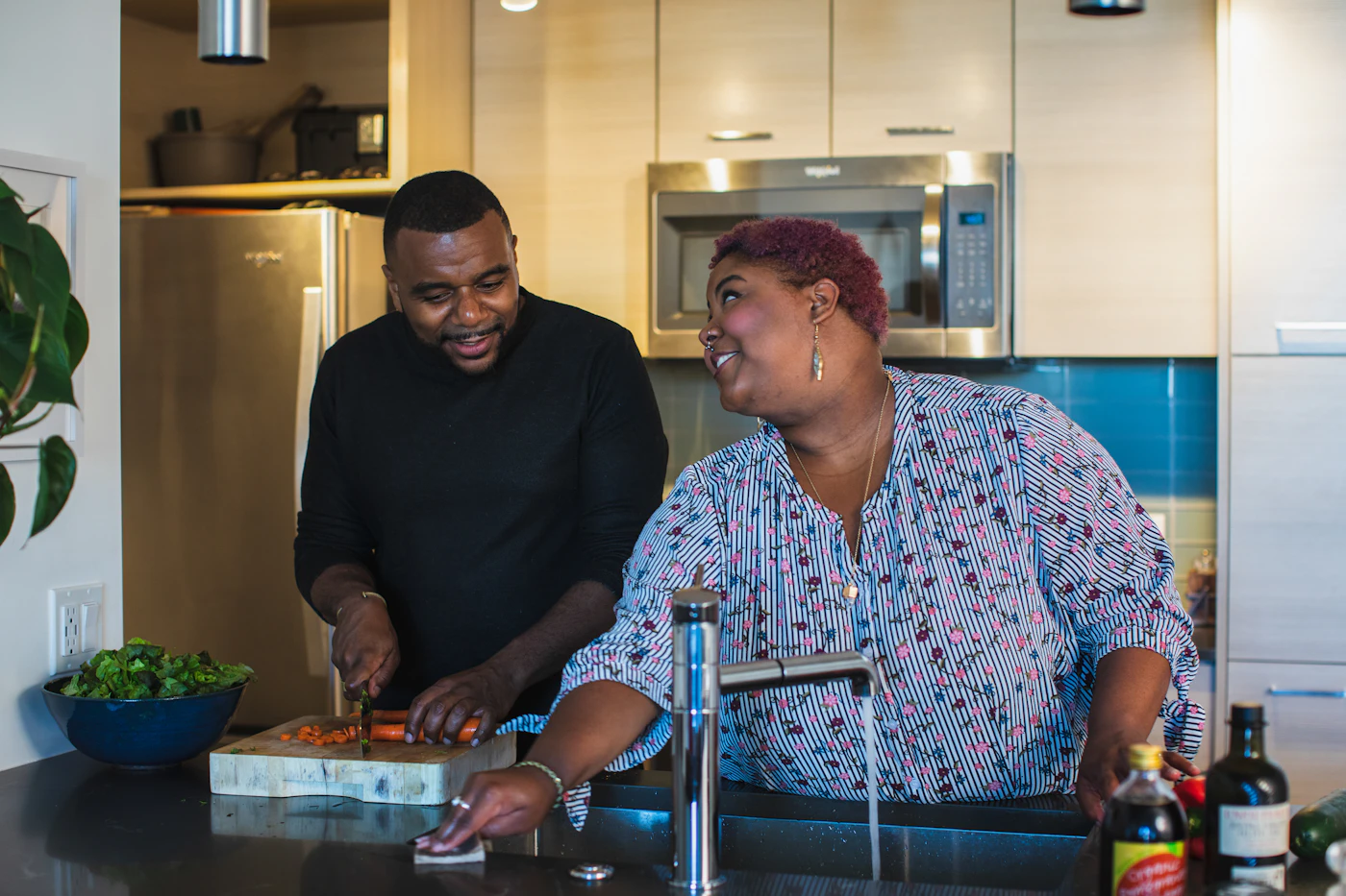 A mother and adult son preparing a meal together at the kitchen sink.